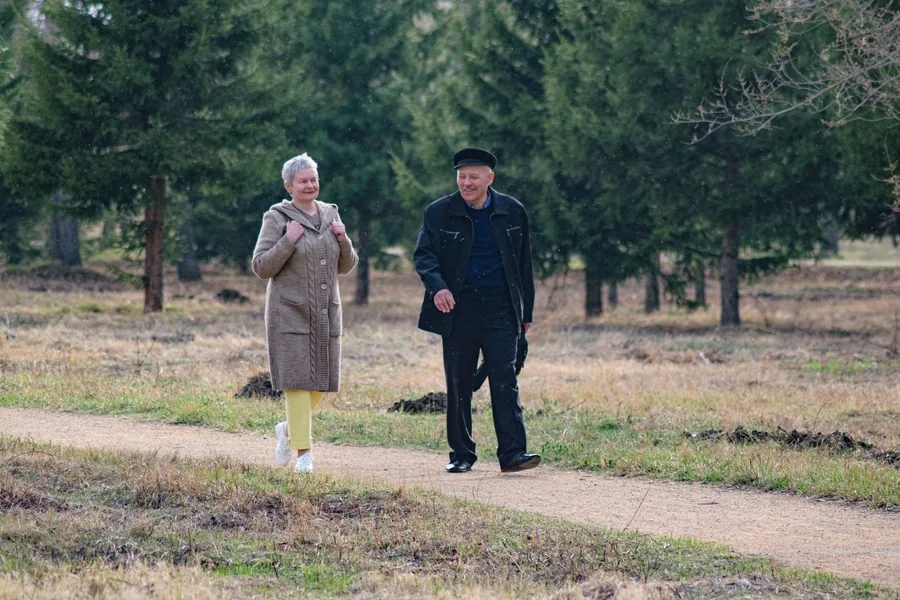 Two older adults walking together along a quiet tree-lined path